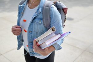 Student holding her textbooks in her arm with a backpack on